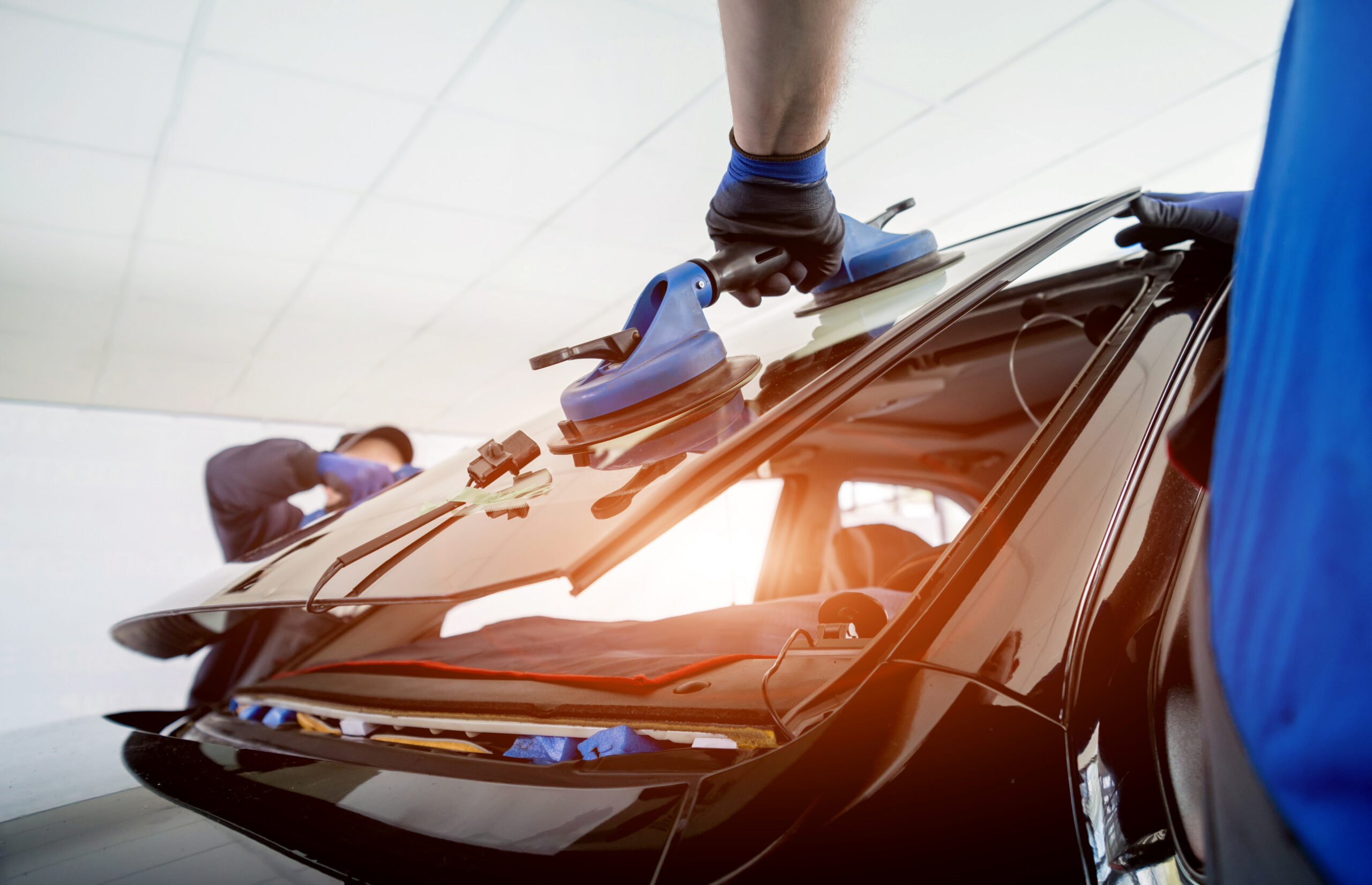 automobile special workers replacing windscreen or windshield of a car in auto service station garage.